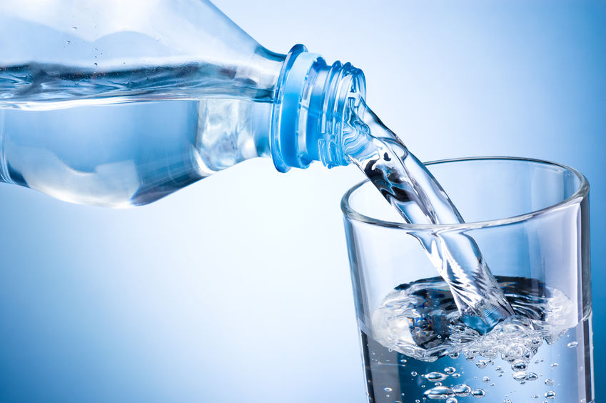 Pouring of table water from bottle into glass on blue background